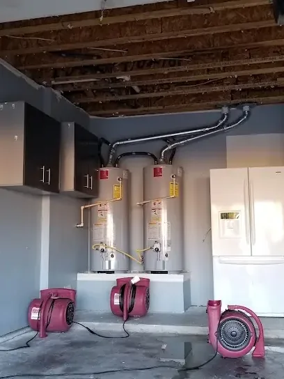 Air movers drying a garage floor below two tank water heaters